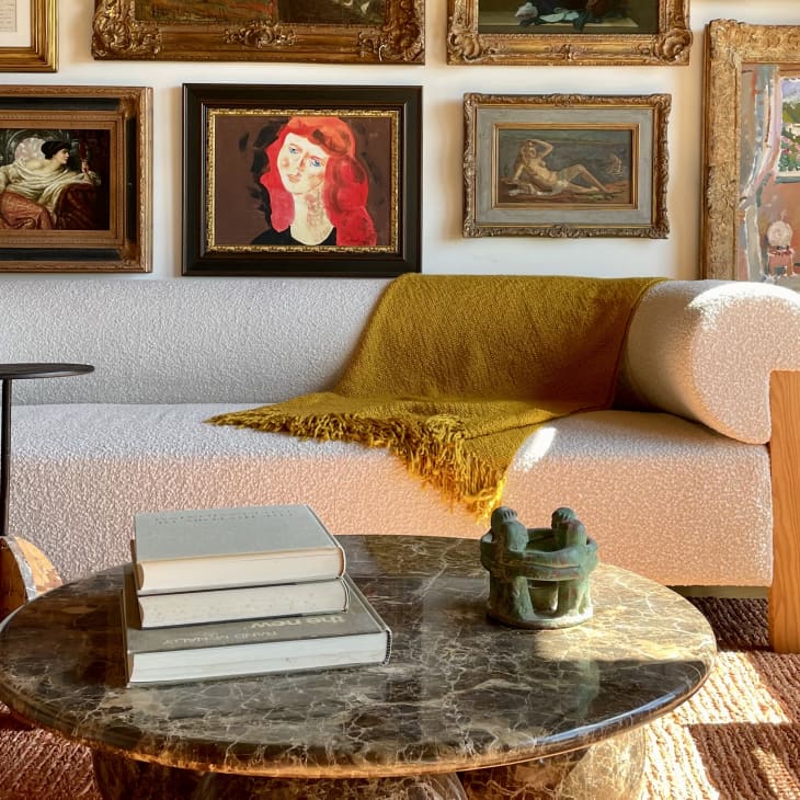 Cozy living room with a white sofa, yellow throw, marble coffee table, and framed art on the wall.