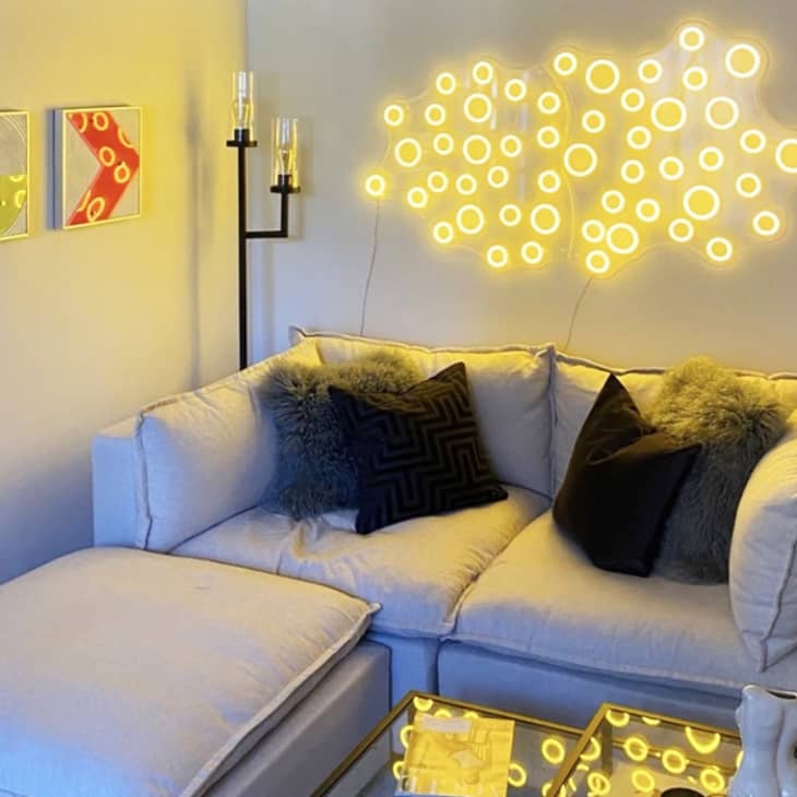 Cozy living room with a beige sectional sofa, geometric pillows, neon wall art, and a glass coffee table.