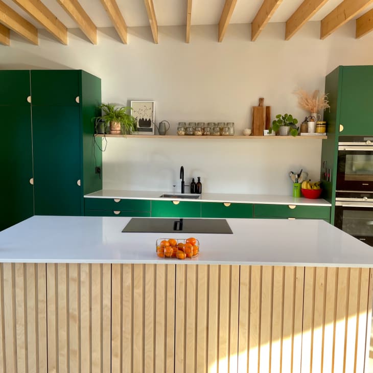 A birch kitchen island with green kitchen cabinets behind