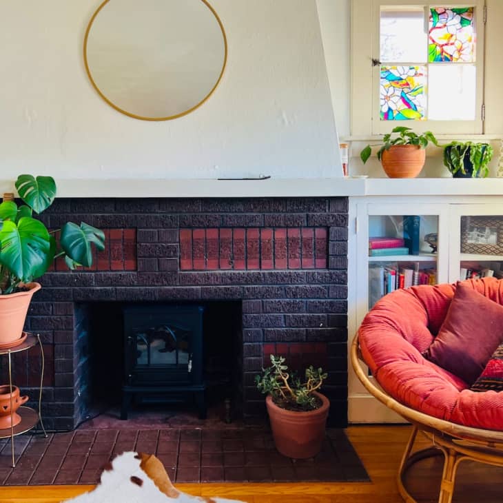 A fireplace with plants next to a red round chair