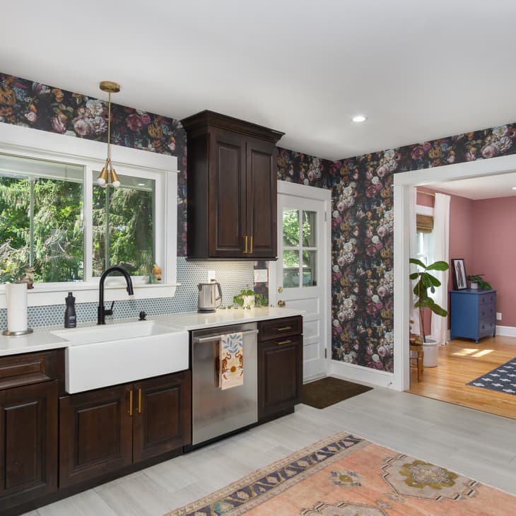 A kitchen with floral wallpaper and dark wooden cabinets