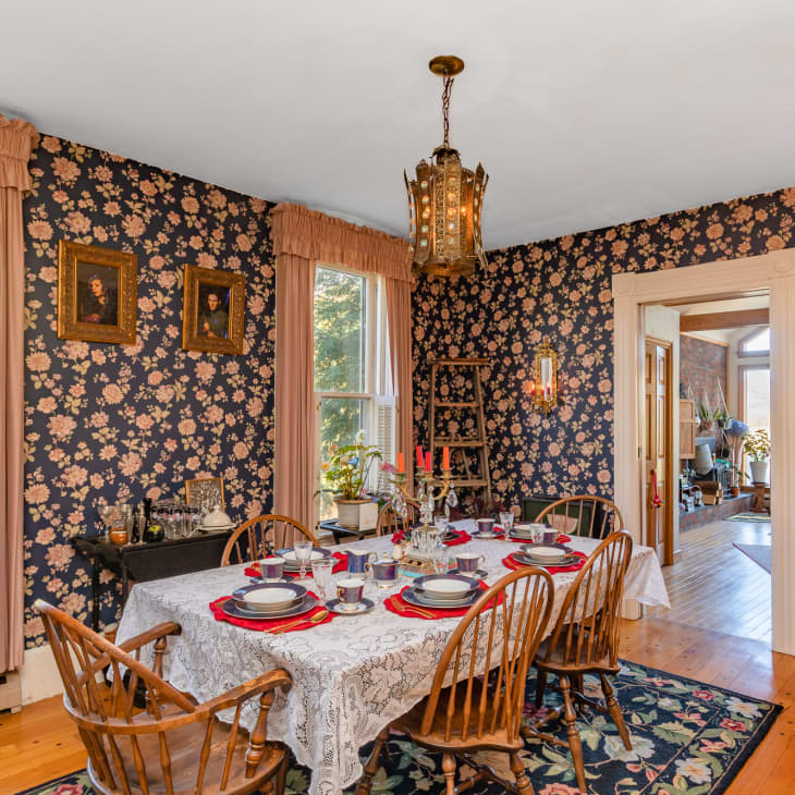 A dining room with floral wallpaper and a table in the center