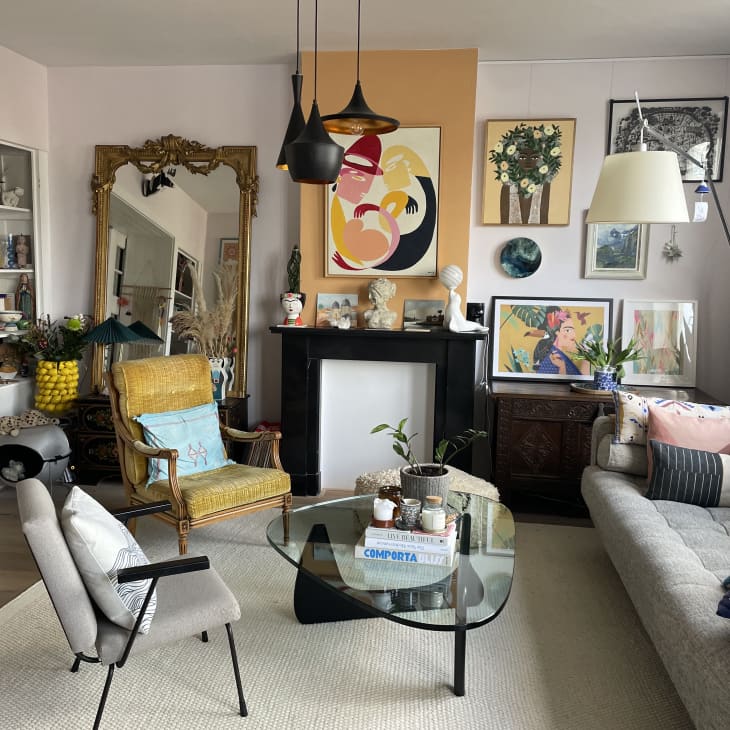 Living room with two arm chairs on one side of glass coffee table and grey sofa on opposite side. Black and gold pendant above coffee table and lots of art work on the walls.