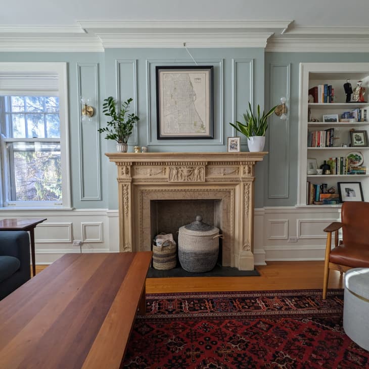 living room with pale blue walls fireplace, built in shelves, plants, navy sofa, rust-colored leather chair