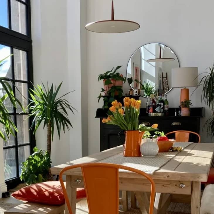 Wooden dining table in sunny room with benches on either side of the table and a orange aluminum dining chair at the head of the table.