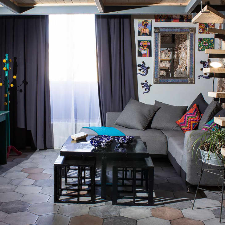 Grey hexagonal lines line living room floor in apartment with grey sectional and wooden staircase.