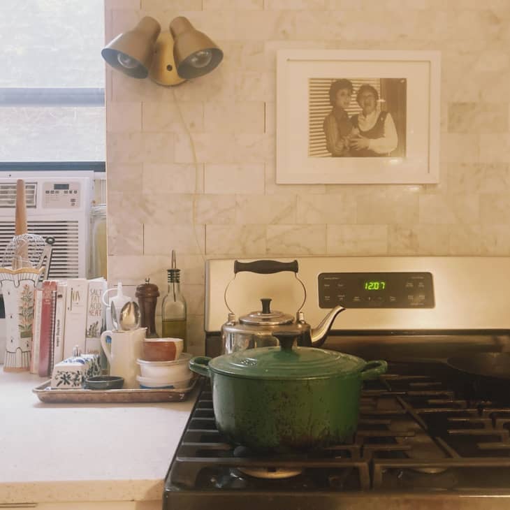 A stove top with a green dutch over, silver teapot, and black cast iron pan on top.