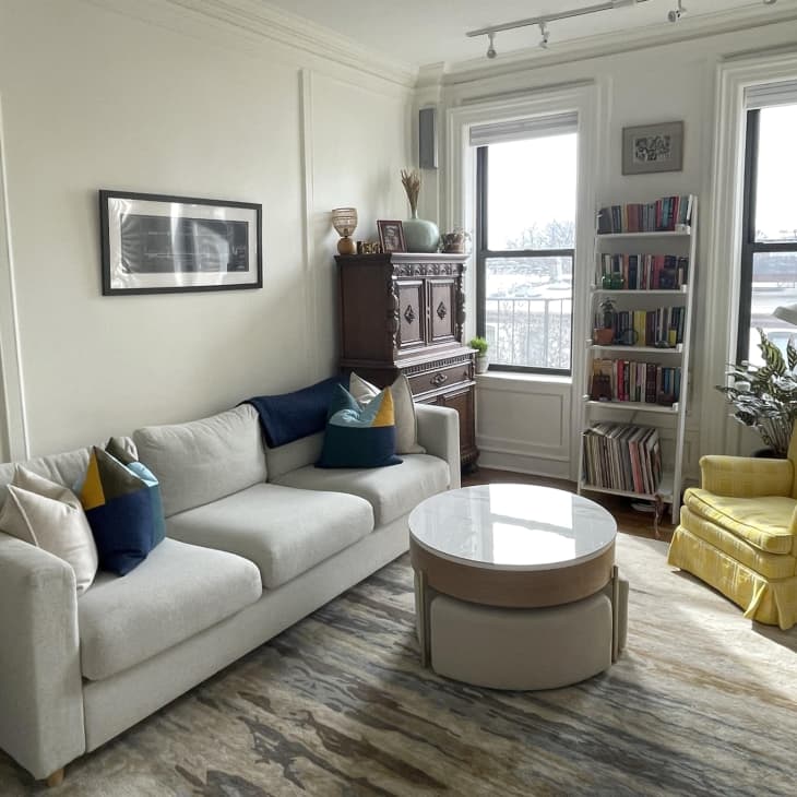 Living roomm with white walls, pale gray sofa, yellow accent chair, round coffee table, tall windows