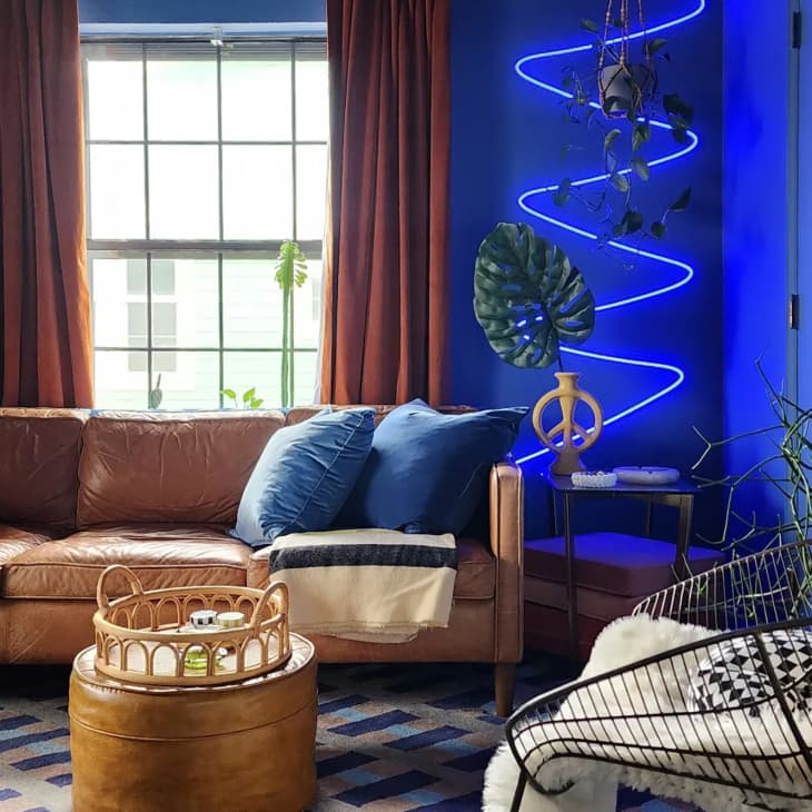 Contemporary living room with brown leather sofa and blue painted walls and a neon squiggle light.
