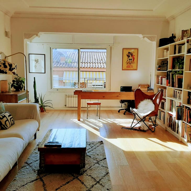 White living room with white sofa, wood floors, and large bookshelves with view into home workspace area