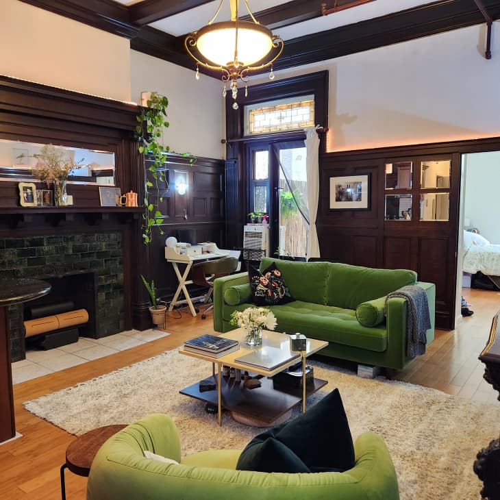 white living room with lots of historic wood details around trim, wainscoting, ceiling beams. Green sofa and armchair