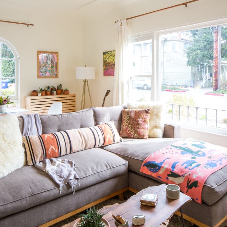 Cozy living room with a gray sectional sofa, colorful pillows, a wooden coffee table, and large windows with garden view.