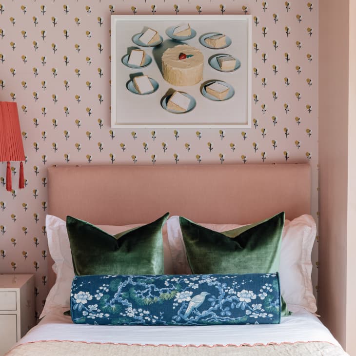 Bedroom with floral wallpaper, green velvet pillows, red lamp, and a shelf displaying colorful handbags.