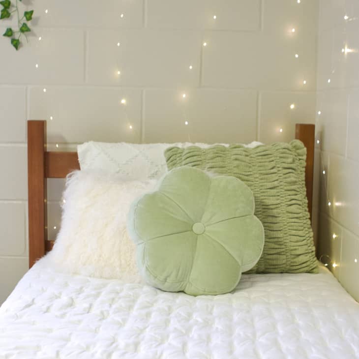 White-painted cinder block dorm room with an elevated bed and green decorative pillows