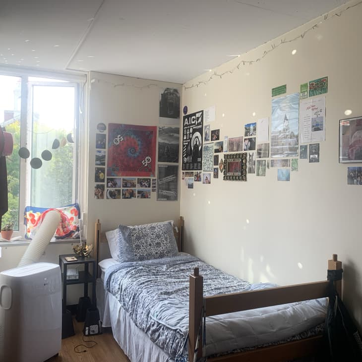 small wood frame bed by a window of off white dorm room with lots of pictures on the walls
