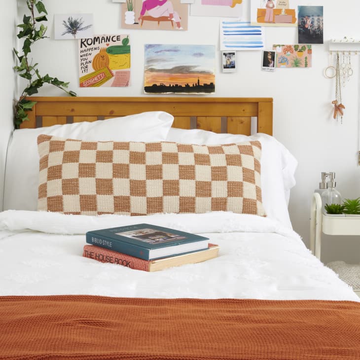 closeup shot of books on a bed with checkered orange and cream pillow behind it - photo gallery wall behind headboard