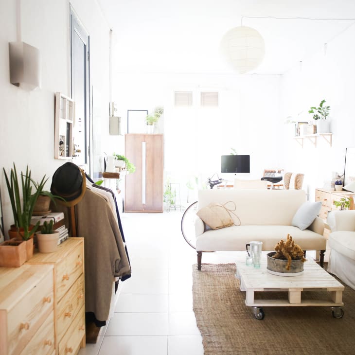 Bright living room with white sofas, wooden furniture, plants, and a wall-mounted shelf.