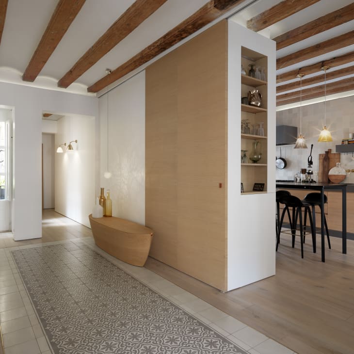 Hallway with patterned tile floor, wooden bench, and open kitchen with pendant lights and bar stools.