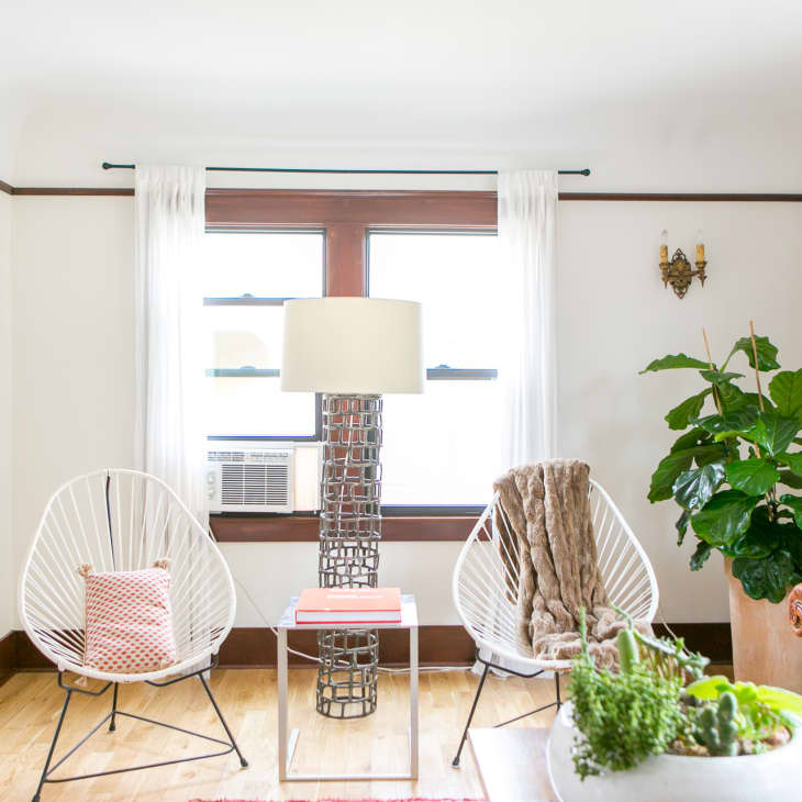 Living room with two white chairs, a large plant, a leather sofa, and a tall lamp by a window with