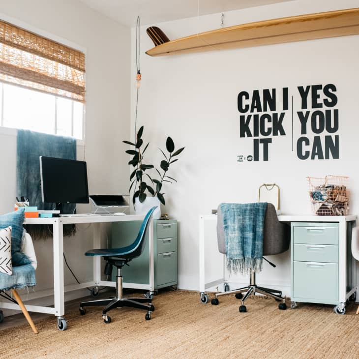 Home office with two desks, chairs, a computer, wall art saying "Can I Kick It Yes You Can," and decorative pillows.