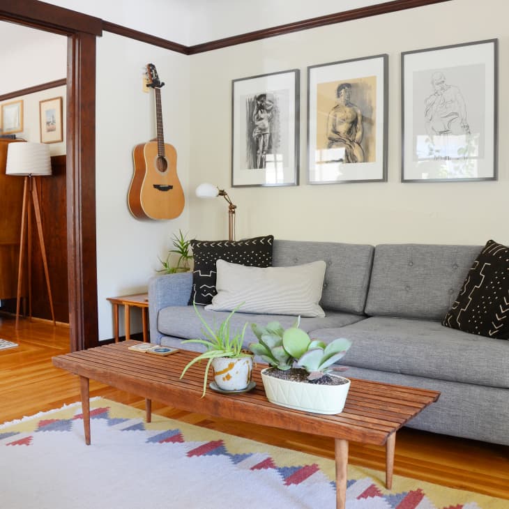 Mid-century modern living room with gray sofa, wooden coffee table, guitar on wall, and framed art above.