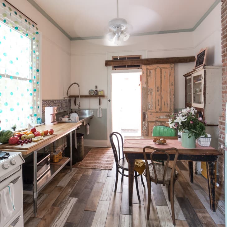 Rustic kitchen with vintage stove, wooden table, mismatched chairs, and a mint green Smeg fridge. Fresh produce on counter.