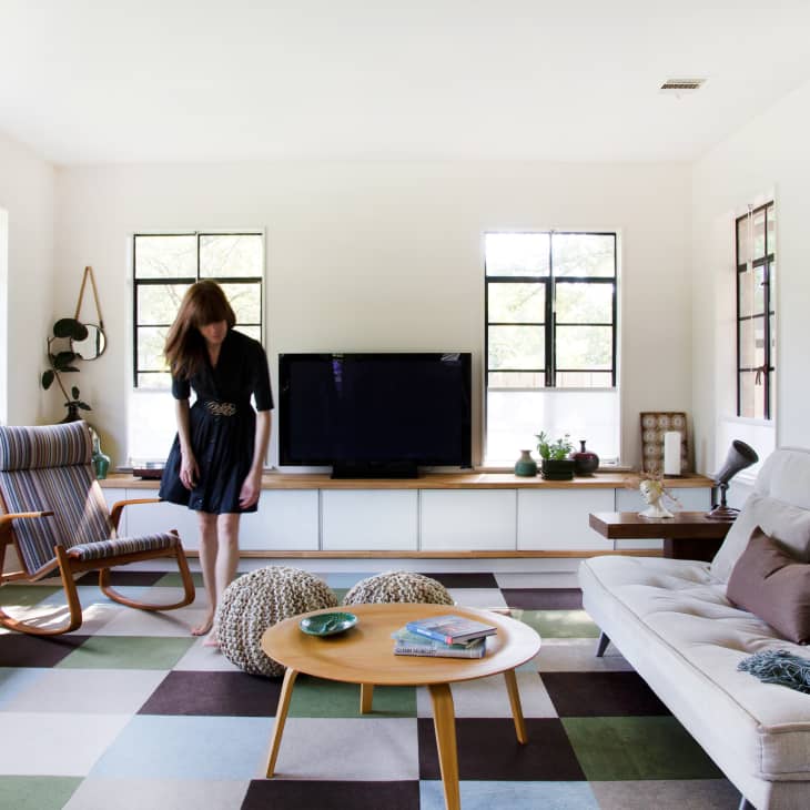 Living room with a woman, beige sofa, striped rocking chair, TV, and colorful checkered rug.