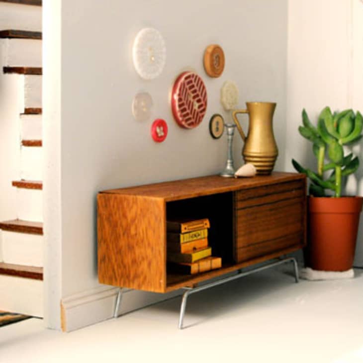 Mid-century modern sideboard with books, gold vase, wall plates, and a potted plant near a staircase.