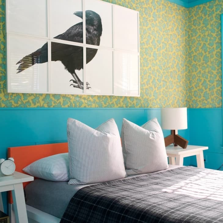 Bedroom with teal and yellow wallpaper, crow artwork, striped pillows, and white bedside tables with lamps.