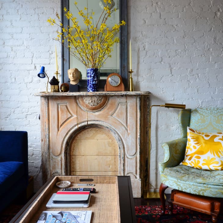 Cozy living room with blue sofa, ornate fireplace, green armchair, and yellow floral pillow.