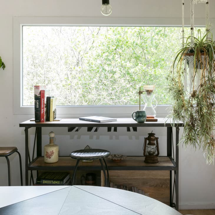 Home office with a window view, books, hanging plant, and a ceramic bust on a desk.