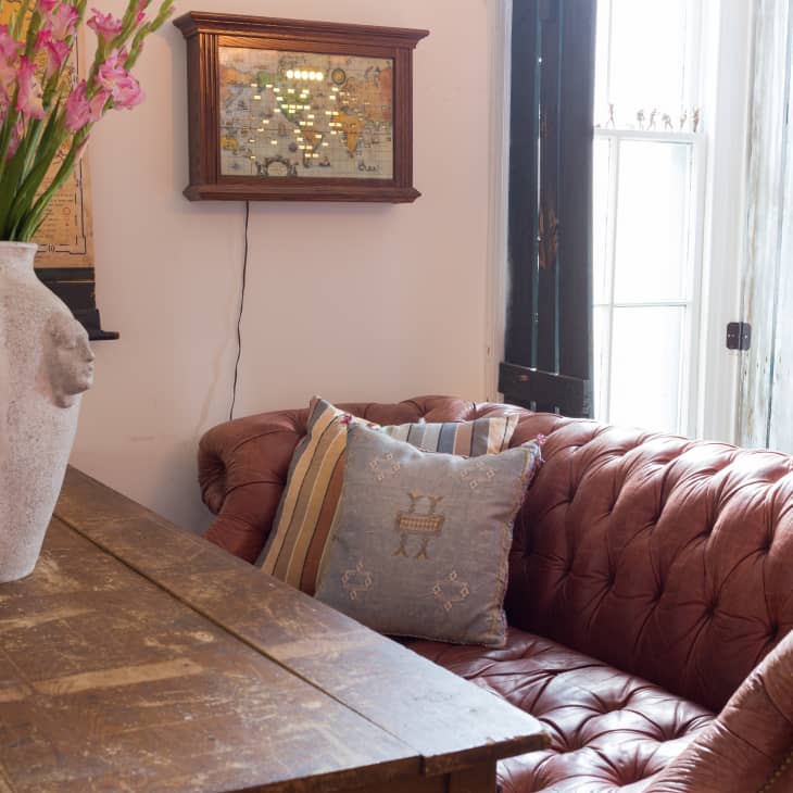 Brown tufted leather sofa with striped pillow, wooden table, large vase with pink flowers, and wall map decor.