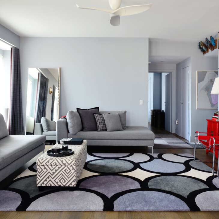 Modern living room with gray sofas, geometric rug, red sideboard, and gallery wall.