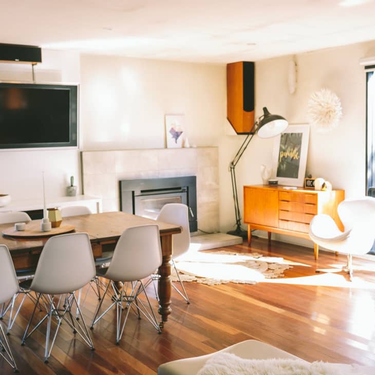 Mid-century modern living room with dining table, white chairs, large TV, floor lamp, and sunlight streaming through a window.