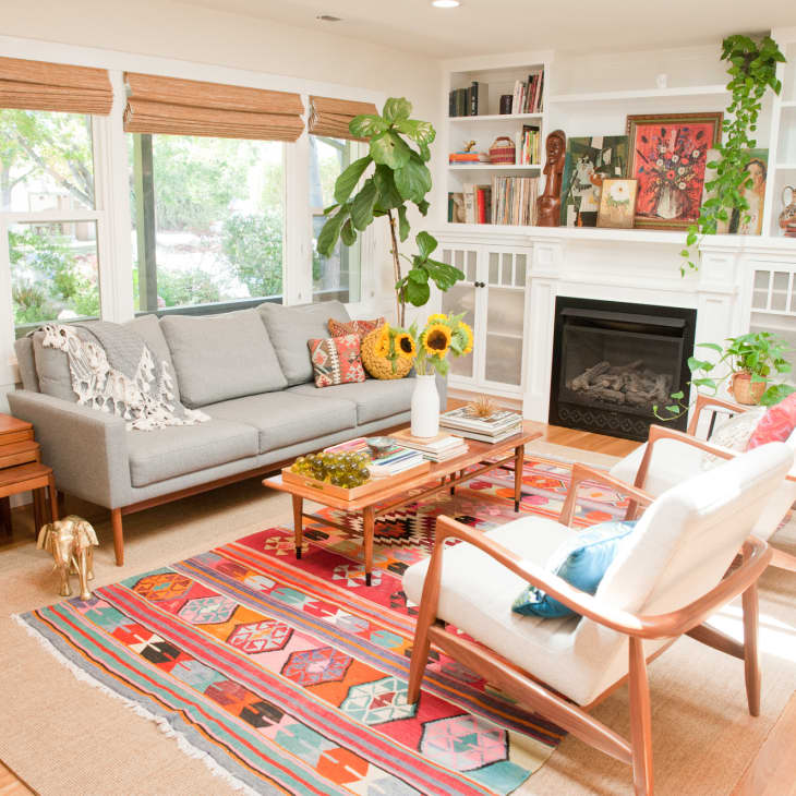 Bright living room with gray sofa, colorful rug, sunflowers on coffee table, and built-in shelves around a fireplace.
