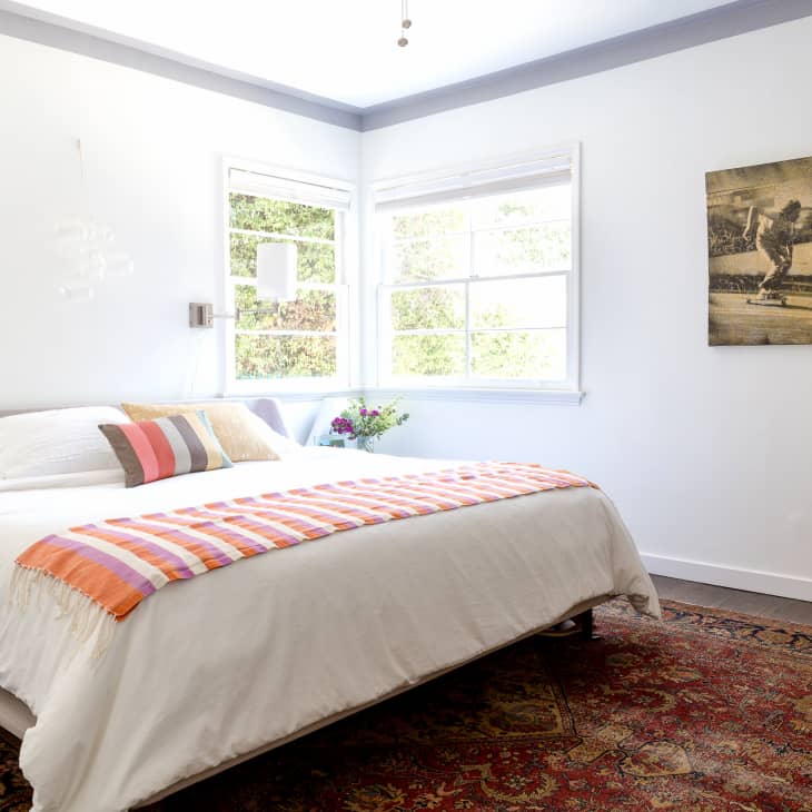 Bright bedroom with a white bed, colorful throw, wall art, and large windows.