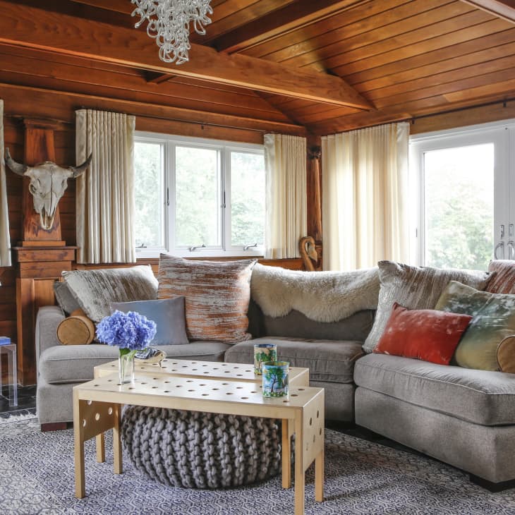 Cozy living room with gray sectional sofa, colorful pillows, wooden ceiling, and a decorative skull on the wall.