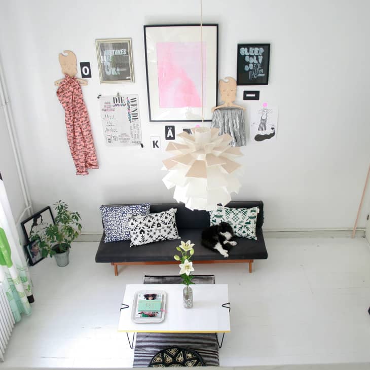 Living room with black sofa, patterned cushions, large white pendant light, wall art, and a small coffee table with flowers.