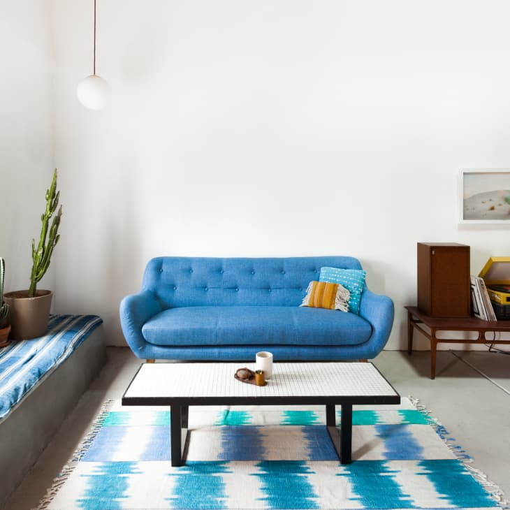 Living room with blue sofa, patterned rug, coffee table, cactus, and record player on a wooden console.