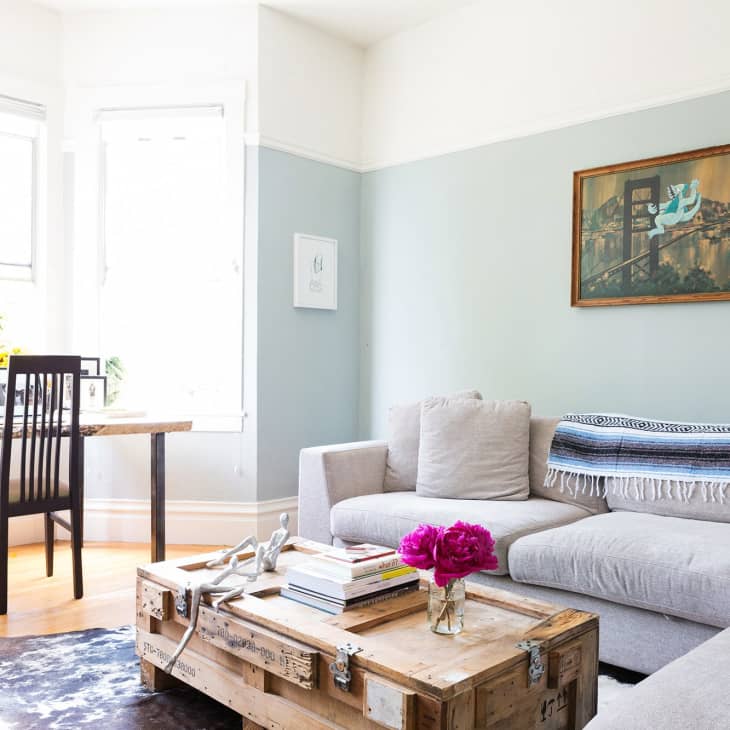 Living room with a gray sectional sofa, wooden coffee table, framed art, and a desk with a chair by the window.