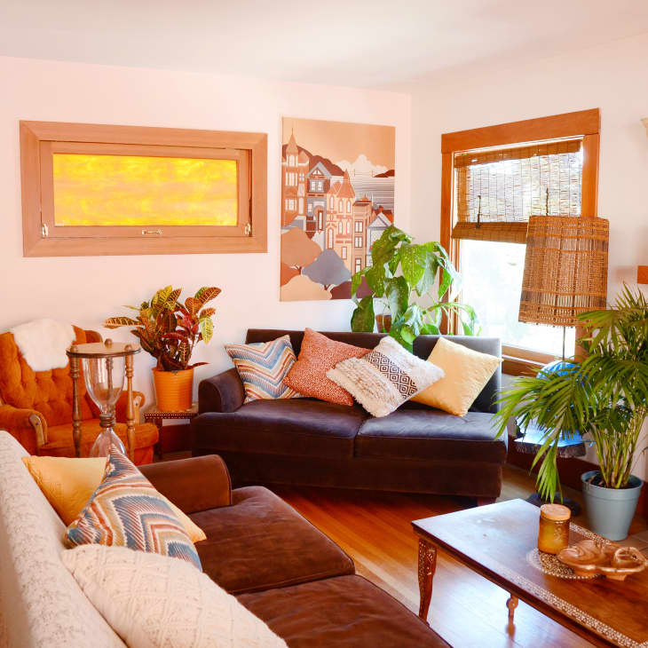 Cozy living room with brown sofas, colorful cushions, plants, a large mirror, and a fireplace.
