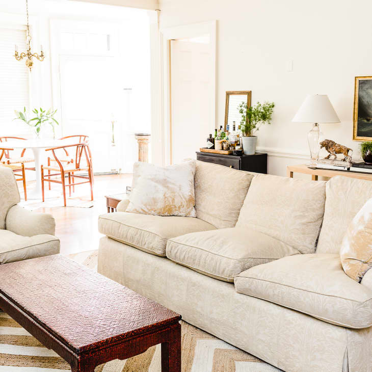 Living room with beige sofa, armchair, wooden coffee table, and dining area with round table and chairs in the background.