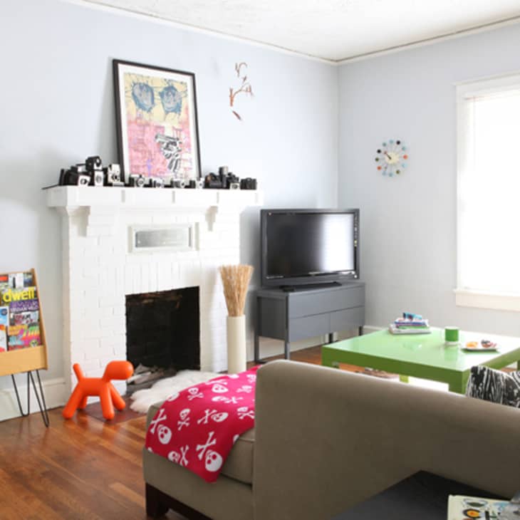 Living room with white fireplace, colorful skateboards, green coffee table, magazines, and a TV on a black stand.