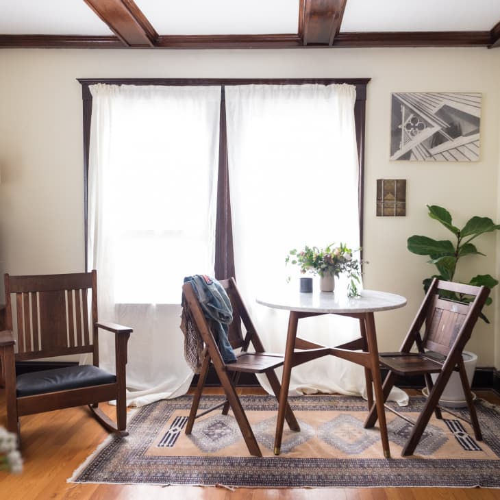 Cozy dining area with a round table, wooden chairs, plants, and framed art on cream walls.