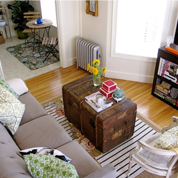 Cozy living room with a gray sofa, vintage trunk coffee table, bookshelf, and yellow flowers in a vase.
