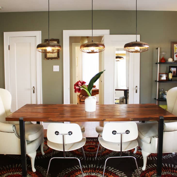 Dining room with wooden table, white chairs, wingback armchairs, pendant lights, and a colorful rug.
