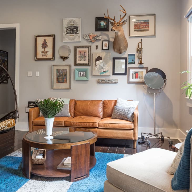Living room with a brown leather sofa, gallery wall, hanging chair, and blue rug.