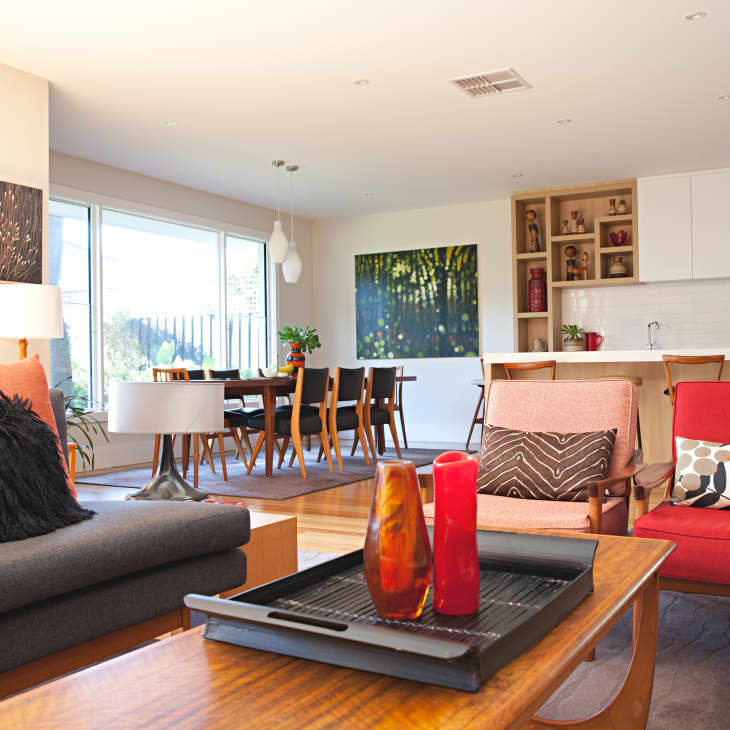 Open-plan living room with red and gray sofas, wooden coffee table, and dining area in the background.