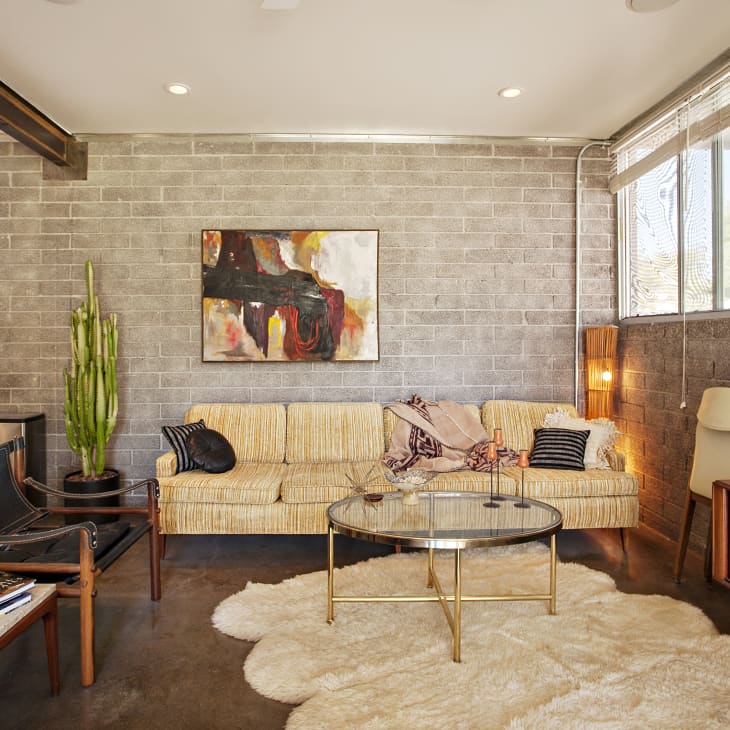 Mid-century modern living room with a striped sofa, abstract art, cactus, and round glass coffee table on a shag rug.