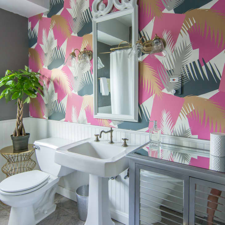 Bathroom with vibrant pink and gray leaf-patterned wallpaper, white sink, toilet, and a potted plant on a wicker stand.